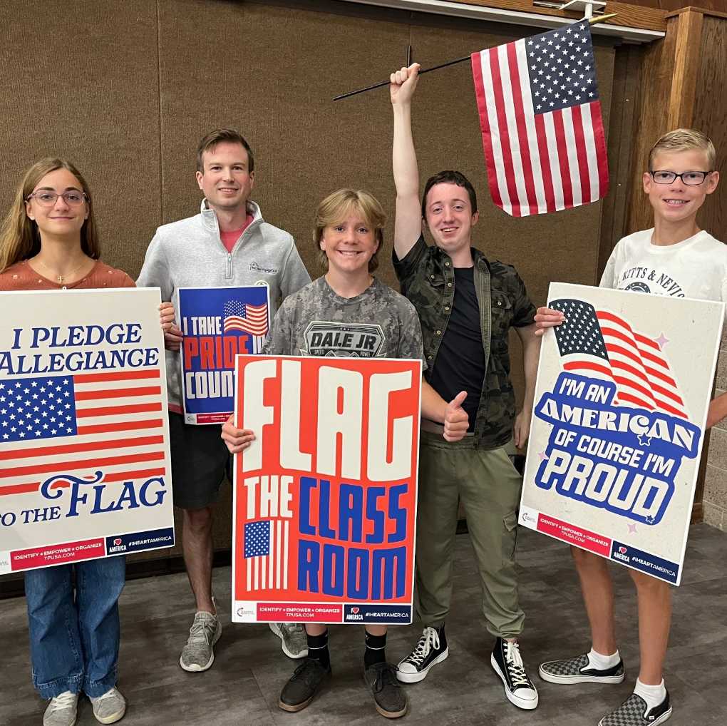 Students and a teacher holding “Flag the Classroom” posters along with a USA flag.