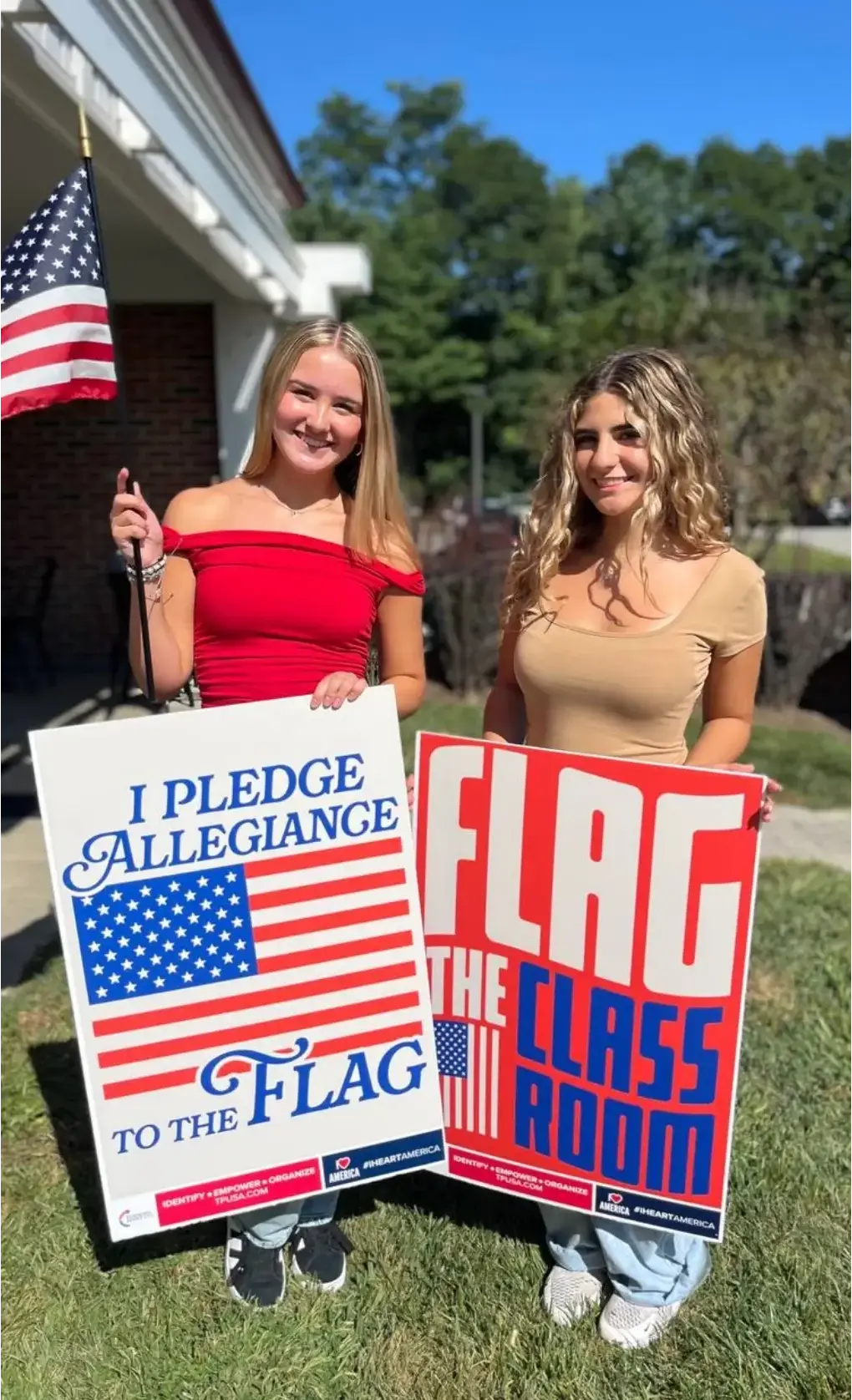 Girls holding “Flag the Classroom” posters along with a USA flag.